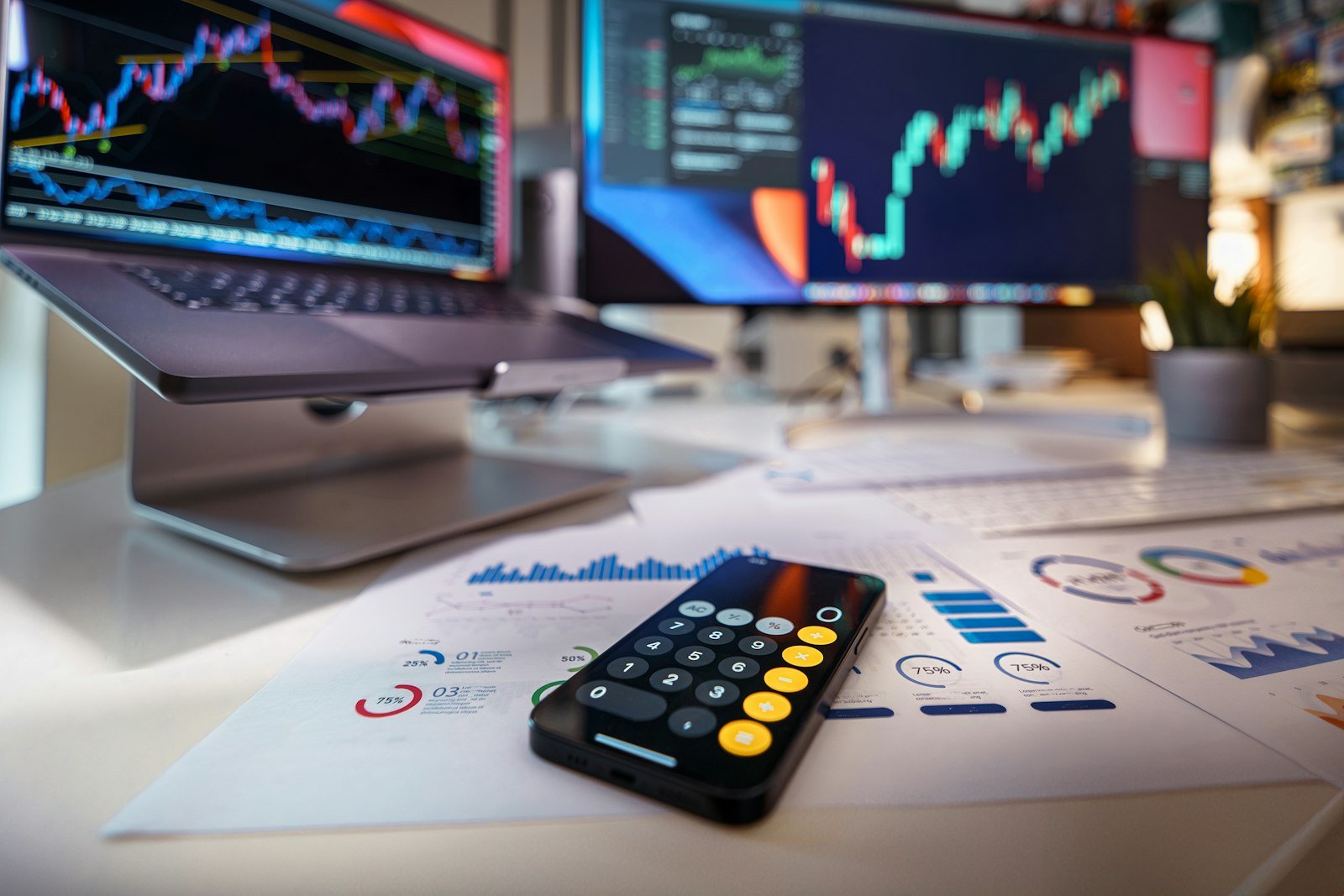 Calculator on a desk with financial charts behind it